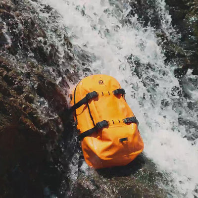 RIVONOVA waterproof backpack tested under waterfall spray and direct sunlight for durable outdoor performance.